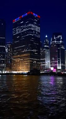 Luminous buildings of New York at the waterfront of the East River. Low angle view at the city skyline at night from the riverscape. Vertical video.