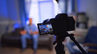 Mavi üniformalı beyaz adam kanepede oturup kamerayla konuşuyor. Kamera görüntüsü doktorun bir blog kaydını görüntüler. Kapatın. Seçici odak.