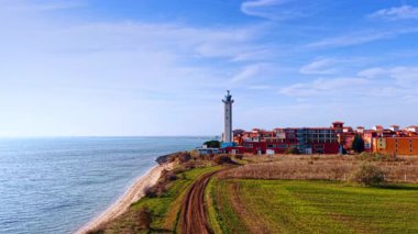 Modern lighthouse and beautiful colorful building on the shore of the Black Sea. Drone rising over the sunny coastal city in Bulgaria.