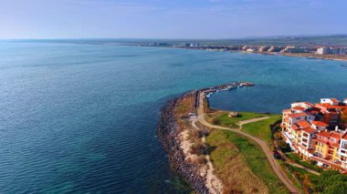Flight over the waterscape approaching the shore with a pier and boats nearby. Rows of colorful organized in a circle in the neighborhood.