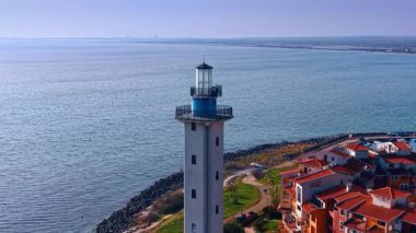 Distancing from a lighthouse against vast peaceful waterscape. Beautiful modern colorful houses are located at the shore.