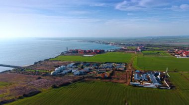 Flight over green fields approaching the sewage treatment plant and farm with solar panels. Waterscape of the beautiful sea at backdrop.