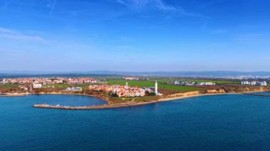 Flight above the blue waterscape of the Black Sea. View on the picturesque city, lighthouse at the coast and long pier.