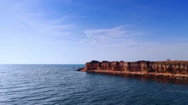 Quick flight over the vast blue waterscape. Approaching the rocky shore with steep cliffs on sunny day.