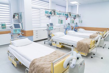 Row of hospital beds in ICU ward. Modern intensive care ward with three hospital beds, blankets and devices arranged for incoming patients.