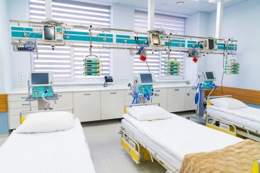 Daytime intensive care ward interior. Row of hospital beds with monitors and drips in bright ICU room