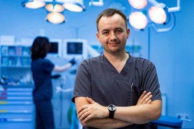 Ameliyathane eldivenli doktor. Eldiven giyen doktor, ameliyat odasında elinde cihazlarla dikiliyor..