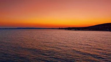 Sunset seascape with calm rippling water. An orange sky reflects gently on the dark sea surface