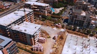 Varna, Bulgaria, 29 June 2025: Construction scene with stacked materials and crane. Building frames rise above pallets of bricks and construction debris in a dusty environment.