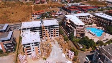 Varna, Bulgaria, 29 June 2025: Construction site next to a bright blue resort pool. The unfinished building and crane stand beside a vibrant hotel with lush green landscaping.