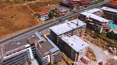 Varna, Bulgaria, 29 June 2025: Elevated scene of resort construction and coastal road. Unfinished structures stand beside finished properties in a dry summer landscape.