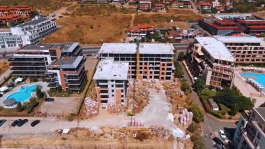 Varna, Bulgaria, 29 June 2025: Construction site between finished resort complexes. An elevated view shows the two unfinished building shells surrounded by existing hotels and pools.