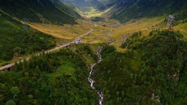 Mountain valley with long waterfall and road. A tall cascading waterfall drops through a deep green valley beside the winding road.