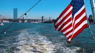 Flag of America on the mast of the boat travelling by the East River. The famous Manhattan Bridge and the Brooklyn Bridge at backdrop.