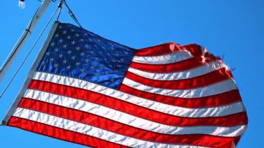 USA flag hanging on the mast flaps in the strong wind. Low angle view. Blue sky at backdrop.