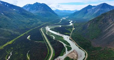 Spectacular valley among the gorgeous mountains crossed by the river lines. A highway goes along the rocks in the wilderness of Alaska, USA. Aerial view.