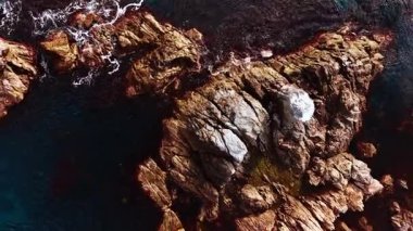 Group of rugged rock islands in clear dark blue water. White foam outlines the edges of the ancient, weathered formations.