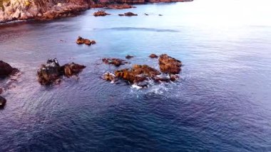 Coastal scene with small scattered rock outcrops. Dark blue water surrounds the formations, creating calm pools and gentle ripples.