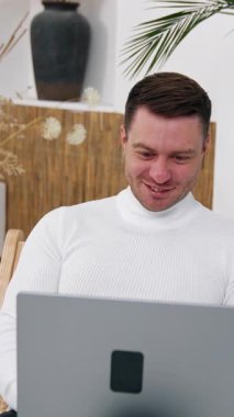 Young male in good humor sitting in front of the computer. Man works at home freelancing. Vertical video