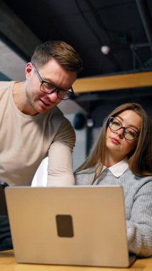 Positive smiling man showing his female colleague something on her computer. Co-working, cooperation and discussion in office. Low angle view. Vertical video