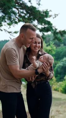 Smiling happy couple hold their baby boy talking to him. Parents of a newborn in nature. Vertical video