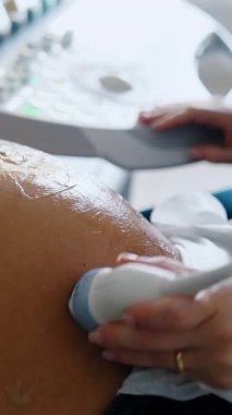 Big belly of a pregnant woman with gel on it. Hand of doctor moves ultrasound device by the patient's abdomen. Close up. Vertical video
