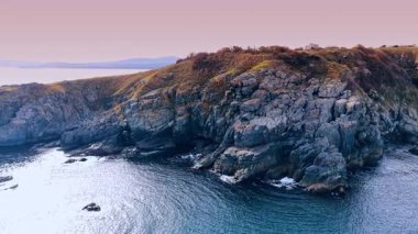 Flight around the grey unapproachable rocks covered with scarce dry vegetation. Beautiful pink sky at backdrop.