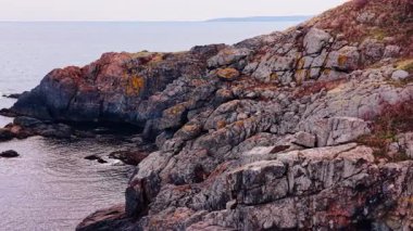 Grey rocks descend into the waterscape. Footage above the rocky shore covered with dry grass.