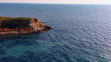 Engebeli mavi sudaki kayalık kıyıya doğru gidiyor. Arkaplanda İHA 'dan gelen uçsuz bucaksız deniz manzarasına bak.