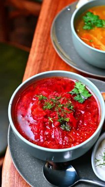 Dereotu garnitürlü kırmızı et suyu. Yanında ekmek ve kremayla servis edilen dereotlu ve maydanozlu koyu kırmızı çorba..