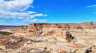 Parlak sıcak güneşin ışığında dik yamaçlı kayalar. Kuru çölün üzerinde kabarık bulutlar olan güzel mavi gökyüzü. Lone Rock Beach Kamp Alanı, Kane County, Utah, ABD.