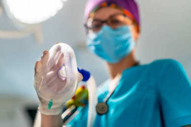 Hemşire anestezi maskesi tutuyor. Hemşire parlak ışık altında düşük açılı bir anestezi maskesi sunar..