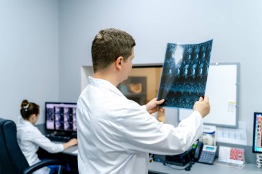 Doktor tarama filmini inceliyor. Meslektaşım ofiste bilgisayar başında çalışırken doktor tıbbi tarama filmi tutuyor..