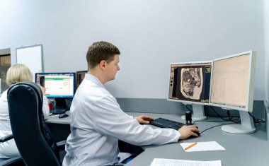 Bilgisayarda çalışan bir doktor. Doktor masada oturup bilgisayar ekranlarındaki tıbbi görüntüleri inceliyor..