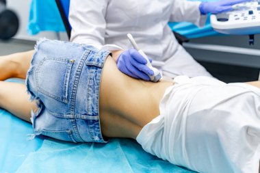 Karında ultrason taraması. Kot şortlu hasta masada yatarken, doktor karnında ultrason yapıyor..