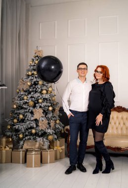 Tatil ağacına yakın bir çift. Aydınlık odada süslü tatil ağacının yanında poz veren çift.
