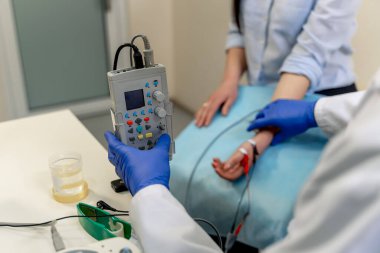 Doktor hasta kolunu elektrotlarla test ediyor. Klinisyen bağlı elektrotlar ve kontrol aygıtı kullanarak kol değerlendirmesi gerçekleştirir.