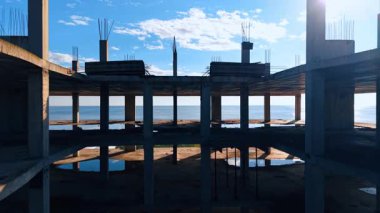 İnşaat halindeki yüksek katlı binanın içine iniyor. Arkaplanda güneşin kamaştırdığı engin mavi deniz manzarası.