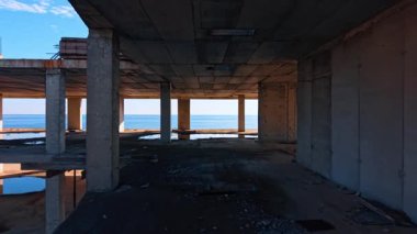 Terk edilmiş, çok katlı binanın içinde. Mavi su manzarası yerdeki su birikintisine yansıyor..