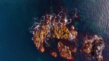 Derin mavi su, su yüzeyinden sarkan kayaları yıkar. İnsansız hava aracı görüntülerinden deniz manzarası.