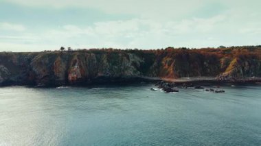 Distancing from the rocky shore of the sea. Drone footage over the peaceful waterscape.