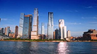 New York, ABD, 1 Ağustos 2025: Güneş gökdelenlere ve nehir manzarasına yansıyor. New York 'un rıhtımının alçak açılı görüntüsü yüksek binaların arasında Gemi Yapısı ile.