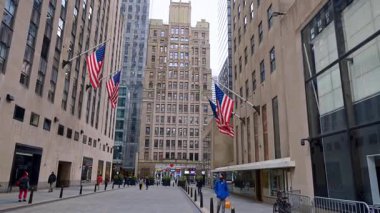 New York, ABD, 22 Ekim 2025: New York gökdelenlerinin gri cepheleri Amerikan bayraklarıyla süslenmiştir. Kalın giysiler giyen insanlar sokakta yürürler..