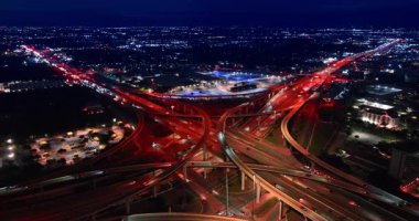 Geceleri modern şehrin uçsuz bucaksız manzarası. Drone kırmızı ışıkla aydınlatılan çok katlı kavşağa iniyor..