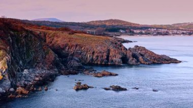 Calm water of the sea at the rocks of the coast. Cityscape on the shore at backdrop. Aerial view.