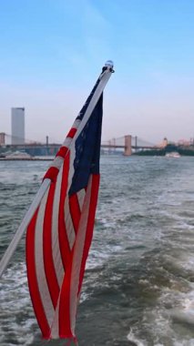 Rüzgarda dalgalanan bir Amerikan bayrağıyla kutup. Teknede nehir manzarası boyunca hareket eden ABD sembolü. Dikey video.