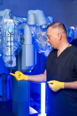 Önlüklü bir cerrah hastane ameliyathanesinde robot cerrahi bir alet gösteriyor. Gelişmiş teknoloji ve temiz yüzey ile ortam parlak..