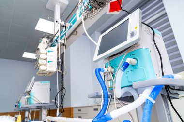 Bir hastane odasında, çeşitli tıbbi makineler hasta bakımını desteklemek için kurulur. Solunum cihazları nefes almaya yardımcı olurken monitörler hayati göstergeler gösteriyor. Ekipman verimlilik için düzenlenmiştir.