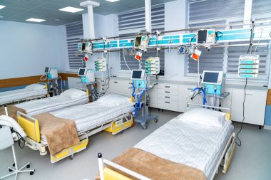 Bir hastane odasında, düzgünce düzenlenmiş birden fazla tıbbi yatak var. Her yatak hastalara yardım etmek için gerekli ekipmanlarla hazırlandı. Oda yumuşak ışıklandırmayla aydınlık..