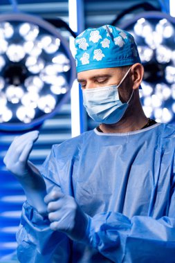 Cerrah modern bir ameliyathanede eldiven giyer. O yaklaşan prosedüre hazırlanırken mavi ışıklar yukarıda parlıyor. Oda ameliyat için hazır..